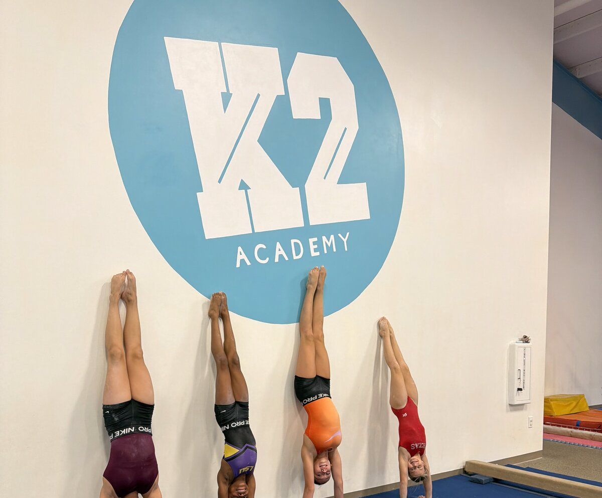 Young gymnasts doing handstands against the K2 Academy logo wall